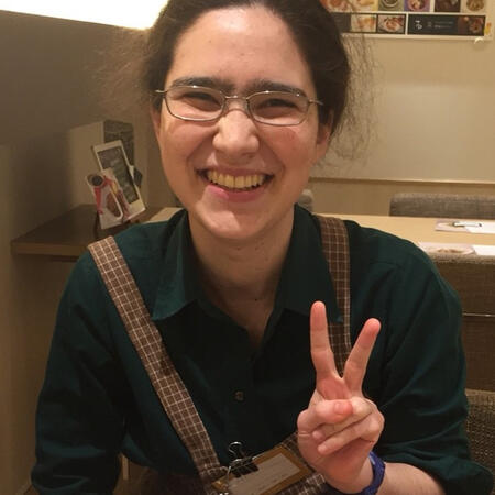 A smiling person in an apron making a victory sign with one hand