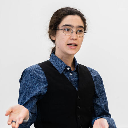 A person in a button-down and vest, gesticulating animatedly.